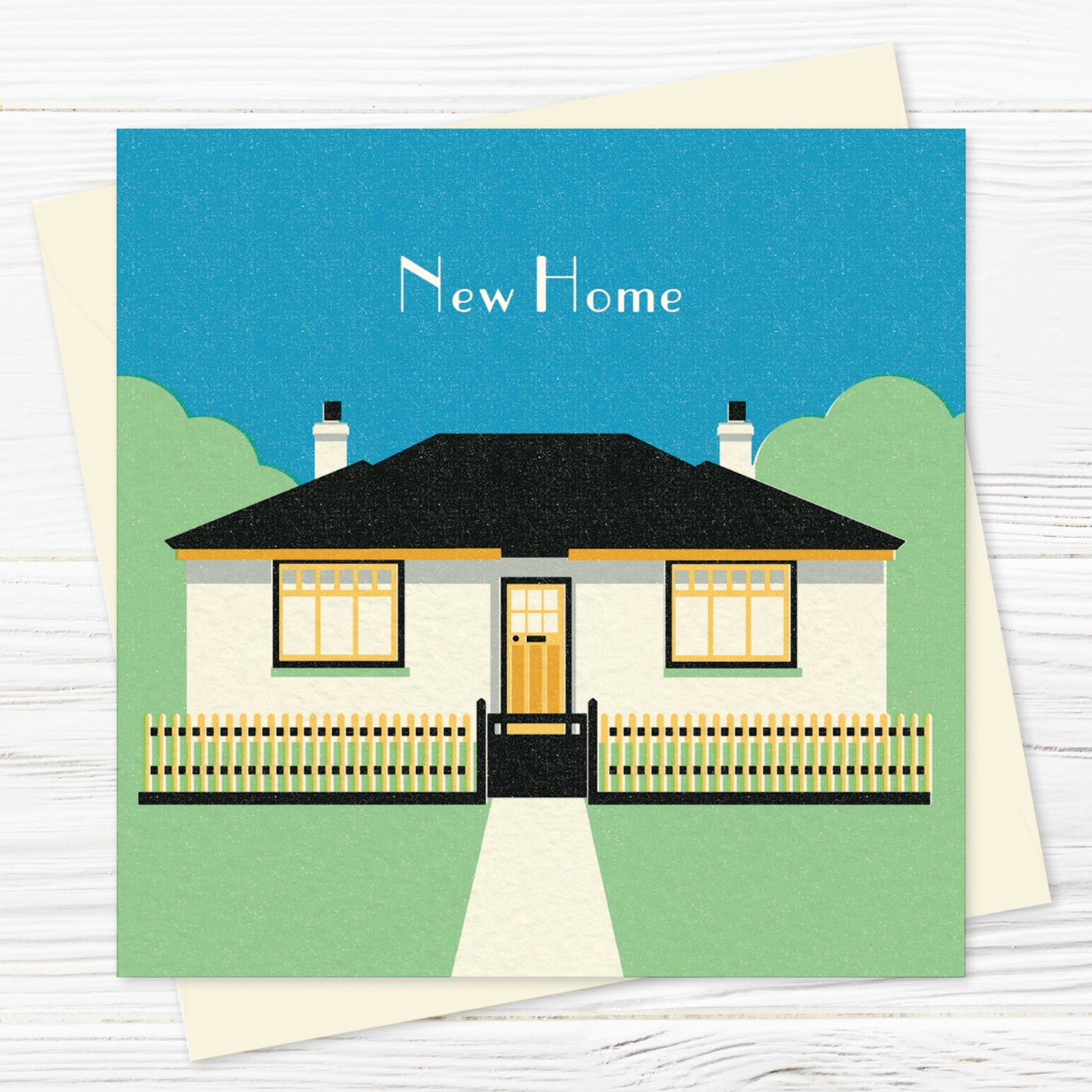 A house warming greetings card and envelope featuring a stylised illustration of a 1930s bungalow and picket fence in green, blue, black and yellow with the words 'New Home' above it. 