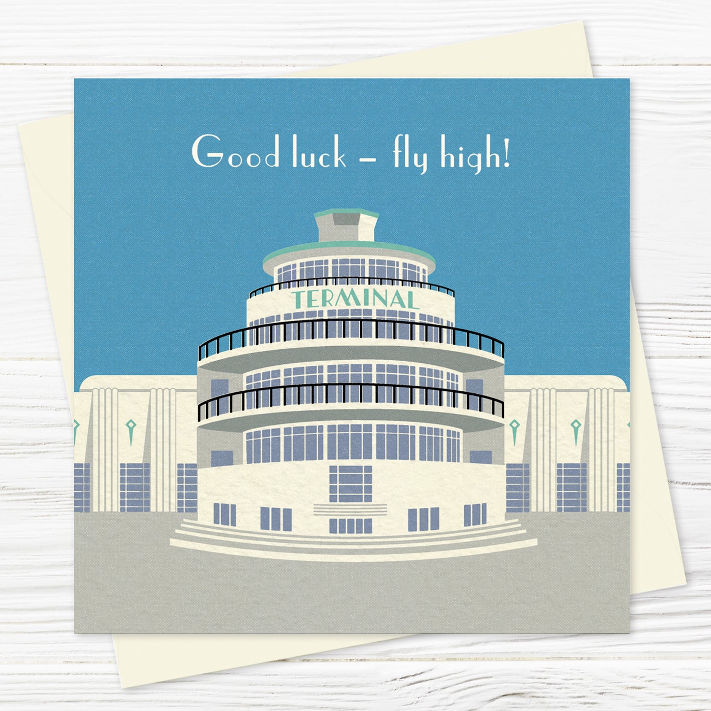 A  greetings card and envelope featuring a stylised illustration of an circular art deco airport building in blue, grey and green with the word 'terminal' across the front of the building. The words at the top say GOOD LUCK - FLY HIGH!