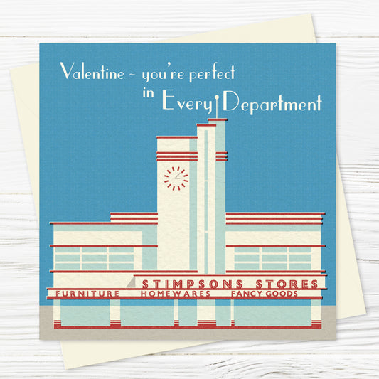 A valentines card and envelope featuring a stylised illustration of an asymmetrical, streamlined building frontage in red and white against a cloudless blue sky. The words STIMPSONS STORES are written across the front, with department names underneath (furniture, homewares, fancy goods), and there is an art deco style clock on the central tower. The words across the top say 'Valentine – you're perfect in every department.'