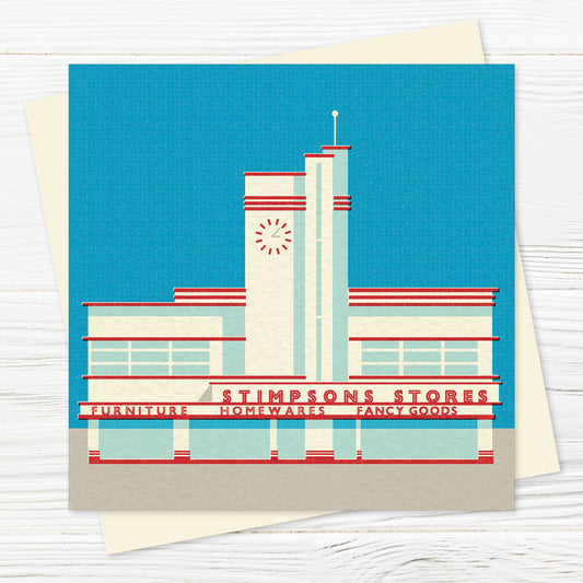 A greetings card and envelope featuring a stylised illustration of an asymmetrical, streamlined building frontage in red and white against a cloudless blue sky. The words STIMPSONS STORES are written across the front, with department names underneath (furniture, homewares, fancy goods), and there is an art deco style clock on the central tower. 