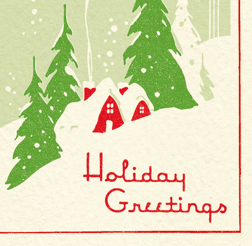 A Christmas card and envelope in red and green featuring a stylised illustration of a cosy house in front of pine trees in a snowy landscape with smoke curling up from the chimney. 